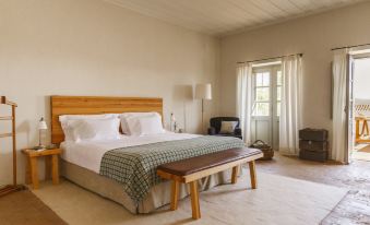 a large bed with a wooden headboard and white linens is in a room with a bench at Sao Lourenco do Barrocal