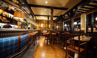 a dimly lit bar with wooden floors , an old - fashioned bar counter , and several stools surrounding it at The Blue Boar
