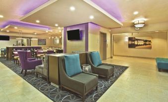 a modern hotel lobby with comfortable seating , a tv , and a dining area , all lit by purple lights at La Quinta Inn & Suites by Wyndham Fairborn Wright-Patterson