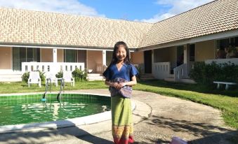a woman in a colorful outfit stands in front of a house and pool with a house on the other side at Baan Kub Doi Mae Chaem