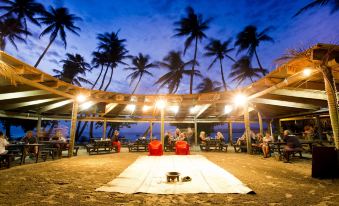 a group of people gathered around a dining table on a sandy beach , enjoying each other 's company at Likuri Island Resort Fiji