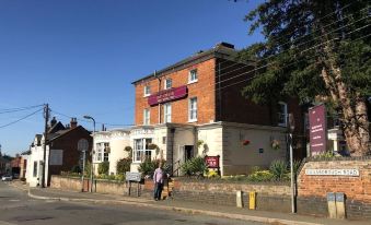 a brick building with a purple sign and flowers on the side , located on a street corner at The Pytchley Inn
