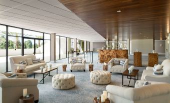 a spacious room with a high ceiling , wooden ceiling beams , and white sofas arranged around a coffee table at Hilton Los Angeles-Culver City, CA