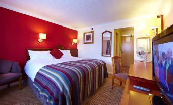 a hotel room with a bed , desk , and chair , along with red walls and wooden flooring at Village Hotel Manchester Hyde