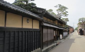 a traditional japanese house with a black roof and wooden walls , surrounded by trees on a street at Just Inn Matsusaka Station