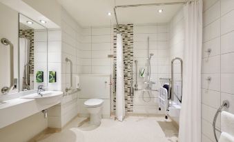 a bathroom with white tiles , a toilet , sink , and shower area , as well as a unique tile design on the walls at Premier Inn Fareham