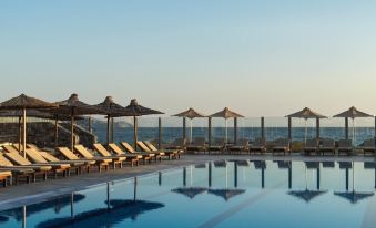 a large swimming pool surrounded by lounge chairs and umbrellas , with the sun setting in the background at Civitel Creta Beach