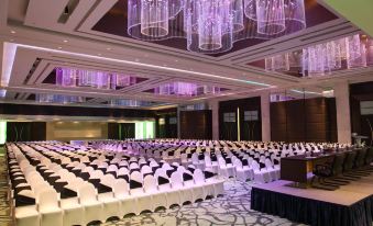 a large conference room with rows of chairs arranged in a symmetrical fashion , under chandeliers and purple lighting at Le Meridien Coimbatore