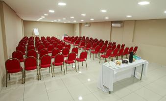 a large conference room with red chairs arranged in rows , a white table at the front of the room , and an air conditioner on the ceiling at Ibis Styles Piracicaba