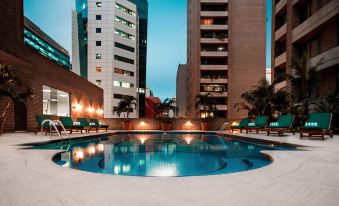 a large outdoor pool surrounded by tall buildings , with lounge chairs and umbrellas placed around the pool area at JW Marriott Hotel Caracas