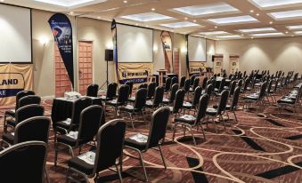 "a conference room with rows of chairs and tables , a projector screen , and an advertisement for "" music lessons "" on the wall" at Novotel Swan Valley Vines Resort