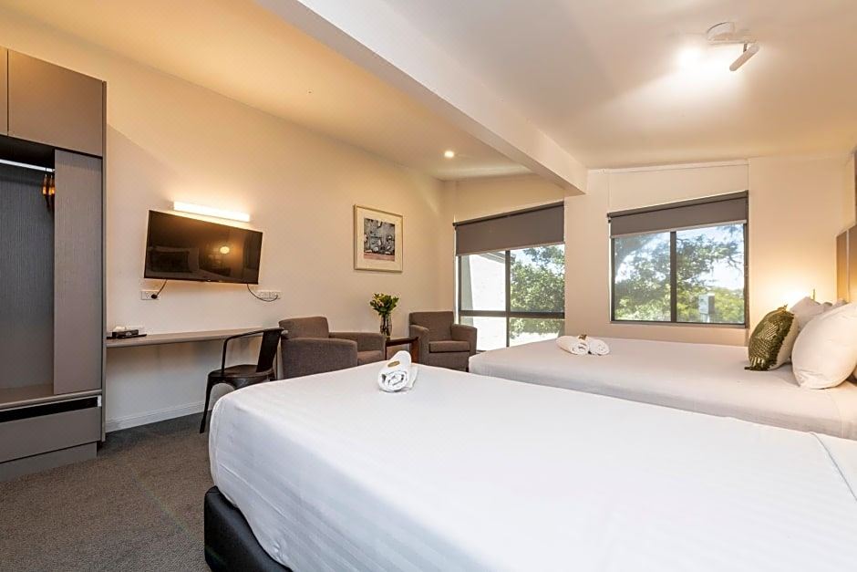 a hotel room with two beds , a tv , and a view of trees outside the window at Fern Bay Motel