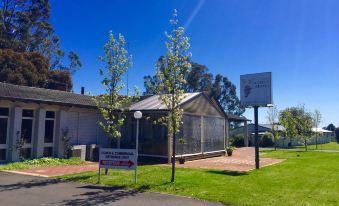 a house with a sign and trees in front of it , surrounded by grass and trees at Manjimup Kingsley Motel