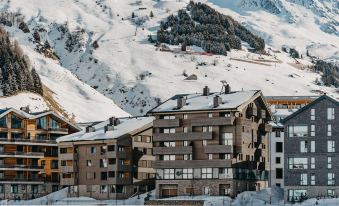 a snow - covered mountain with a row of buildings , possibly a hotel , surrounded by trees and mountains at Radisson Blu Hotel Reussen Andermatt