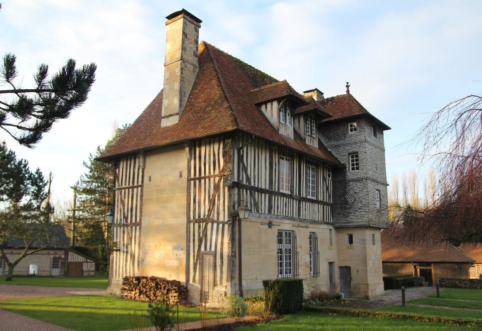 a large stone house with a red tile roof and chimneys , surrounded by trees and grass at Les Manoirs des Portes de Deauville - Small Luxury Hotel of the World