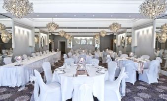 a large , well - decorated banquet hall with multiple dining tables set for a formal event , white tablecloths , and chandeliers at Thornton Hall Hotel & Spa