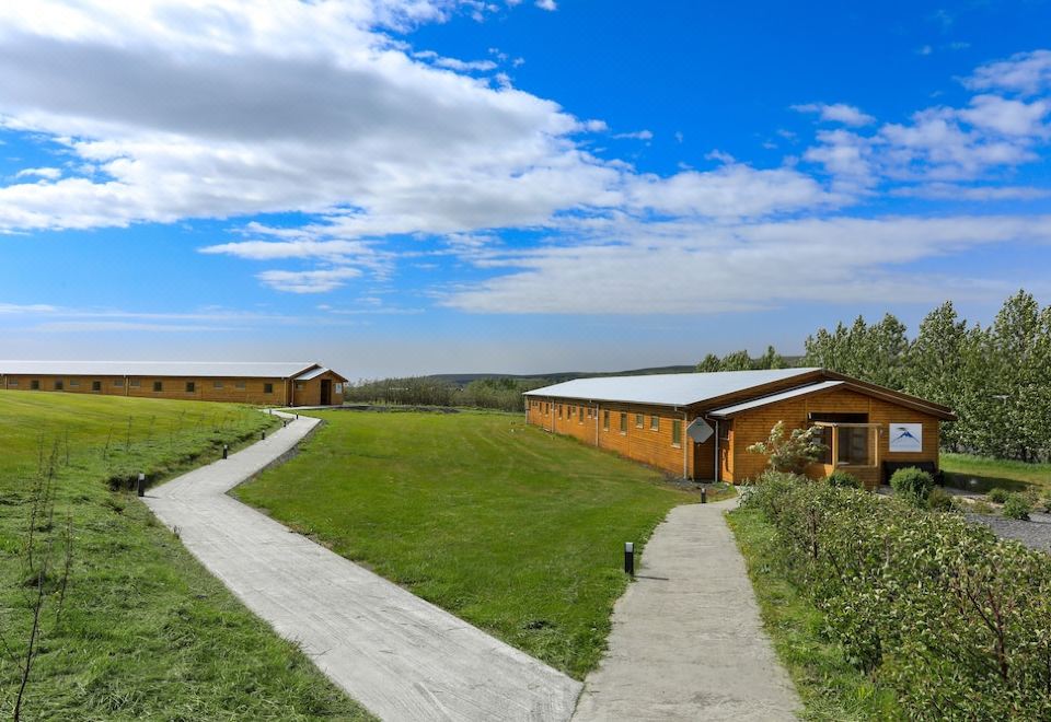 a grassy field with two wooden buildings , one on the left side and the other on the right side of the field at Hotel Eyjafjallajokull