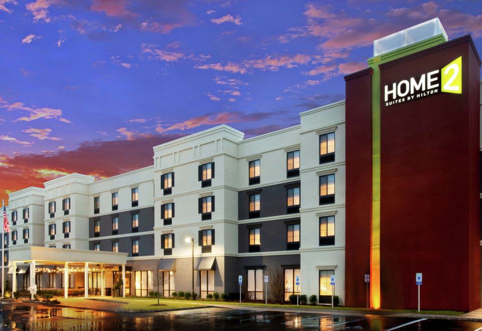 "a modern hotel building with the name "" home 2 suites "" on its side , illuminated by street lights at dusk" at Home2 Suites by Hilton Long Island Brookhaven