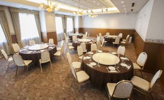 a large , well - decorated banquet hall with multiple round tables and chairs set up for a formal event at Hotel JAL City Aomori