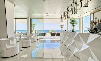 a modern , white - themed hotel lobby with large windows offering views of the ocean and trees at The Ivi Mare - Designed for Adults by Louis Hotels