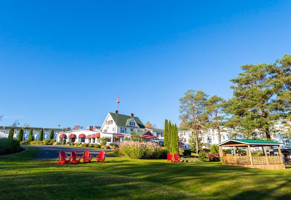 a large white house with a flag on top is surrounded by a lawn and red chairs at Auberge Gisele's Inn