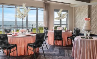a room with several round tables covered in pink tablecloths , surrounded by chairs and adorned with flowers at Aloft Ocean City