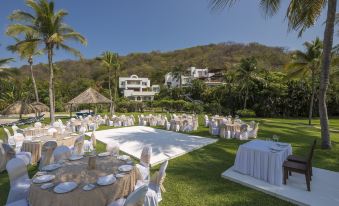 a large outdoor event space with tables , chairs , and flowers is set up in a tropical setting at Camino Real Zaashila Huatulco