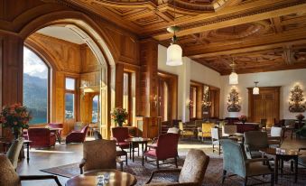 a large , elegant hotel lobby with wooden paneling , high ceilings , and multiple chairs arranged in a comfortable seating area at Badrutt's Palace Hotel