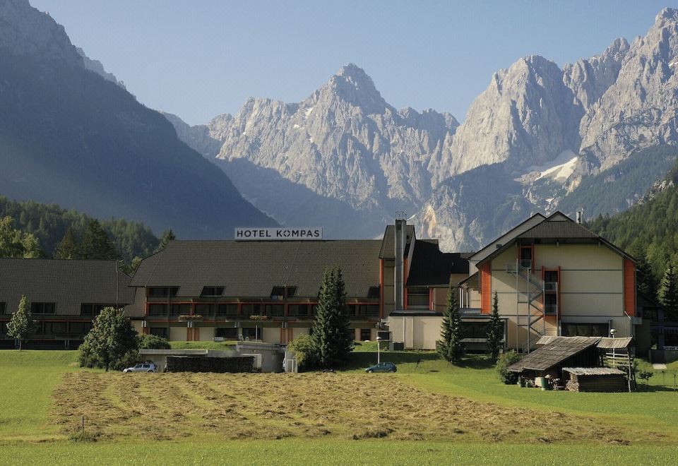 a large building with a sign on the side is situated in front of a mountain range at Hotel Kompas