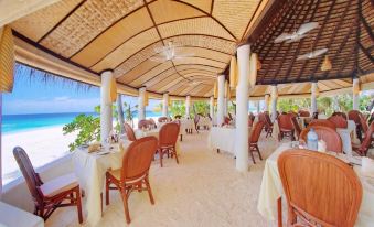 a large dining room with wooden tables and chairs , covered by a thatched roof , overlooking the ocean at Angaga Island Resort & Spa