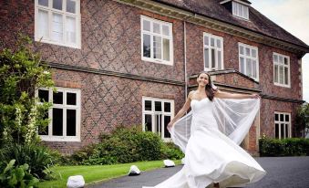 a woman in a white wedding dress is walking on the driveway of a brick building at Mercure Goulburn