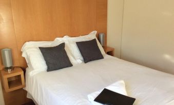 a bed with white sheets and two black pillows , a wooden headboard , and a black tablet on top of it at Coach House Hotel