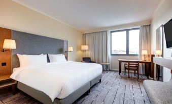 a large bed with white linens is in a room with a window and desk at Radisson Blu Waterfront Hotel, Jersey