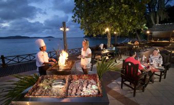 a group of people are enjoying a meal at a waterfront restaurant , with a variety of food and drinks on the table at Perhentian Island Resort