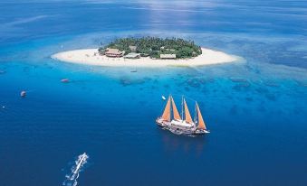 a sailboat with orange sails is sailing on the ocean near a small island , surrounded by clear blue water at Beachcomber Island Resort