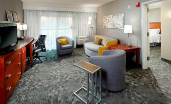 a modern hotel room with gray sofas , wooden table , and white curtains , along with other furniture and lighting at Courtyard Akron Stow