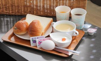 a breakfast tray with bread , eggs , and coffee is placed on a wooden surface , accompanied by a basket containing tea bags at Toyota Village