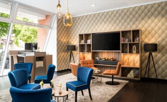 a modern living room with blue chairs , a television , and a large screen on the wall at Leonardo Hotel Berlin