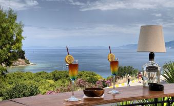 two glasses of drinks on a balcony with a view of the ocean and mountains in the background at Hotel Carina