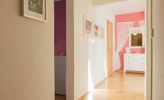 a long , narrow hallway with hardwood floors and white walls , leading to a bedroom with a pink bed at Garden Apartment