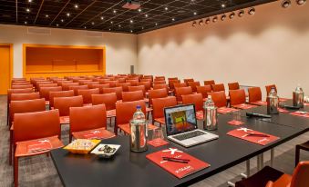 a conference room with red chairs , tables , and a laptop on a table , ready for a meeting or presentation at Glam Milano
