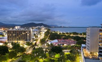 a city skyline at dusk , with buildings and trees illuminated by lights , as well as a large group of people gathered in front of a building at Pacific Hotel Cairns