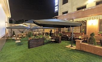 an outdoor dining area with several tables and chairs , surrounded by grass and lit up at night at Alma