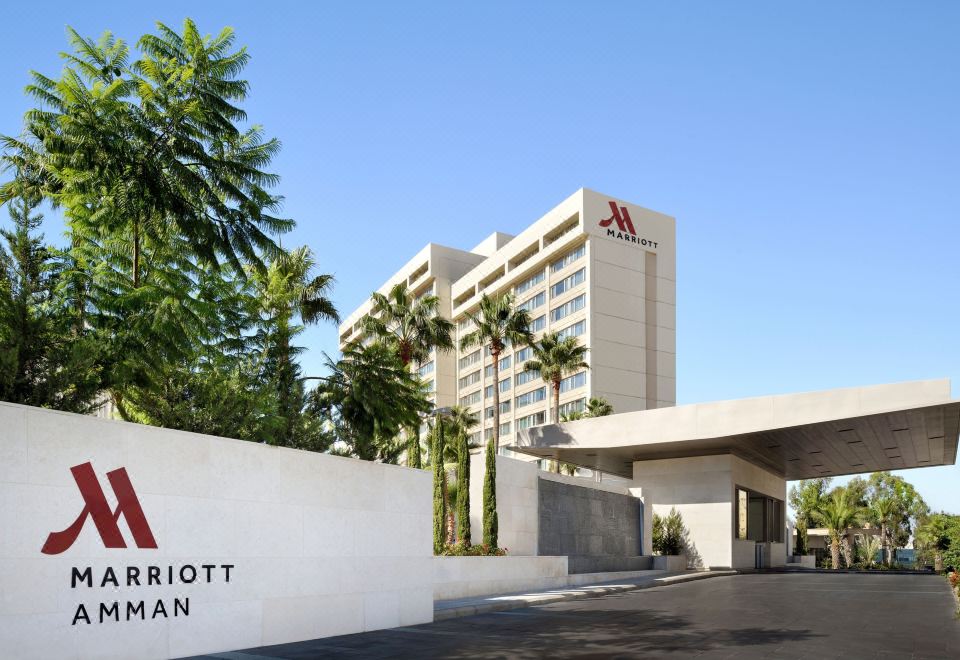 "a large hotel with a sign that says "" marriott "" in front of it , surrounded by palm trees" at Amman Marriott Hotel
