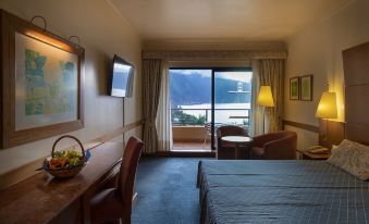 a hotel room with a bed , desk , and chair near a sliding glass door that leads to a balcony overlooking a lake at Monte Mar Palace Hotel