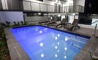a large swimming pool with blue water and several lounge chairs is surrounded by a building at Pacific Sands Apartments Mackay