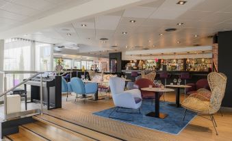 a modern lounge area with colorful chairs , tables , and a bar , providing a comfortable atmosphere for guests at Novotel Dijon Sud
