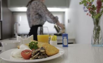 a woman in a kitchen preparing a meal , with a plate of food on the counter and a knife on the table at Room Motels Gympie