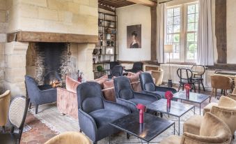 a cozy living room with a fireplace , several chairs and couches arranged around it , and a coffee table in the center at Les Manoirs des Portes de Deauville - Small Luxury Hotel of the World