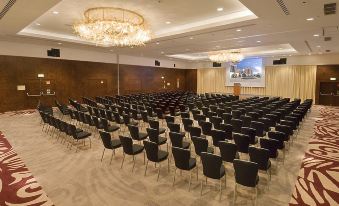 a large conference room with rows of black chairs and a chandelier hanging from the ceiling at Hilton Vilamoura As Cascatas Golf Resort & Spa